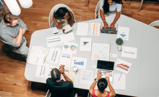 4 individuals with another standing around a table working on a brainstorming event