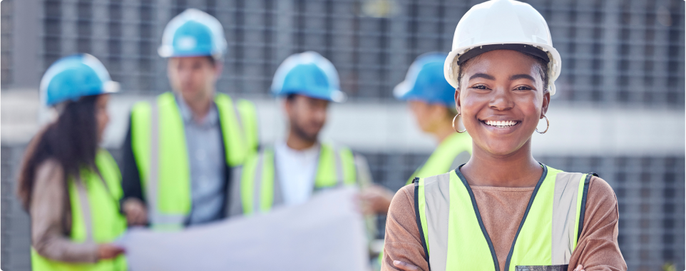 Woman in construction attire smiling with colleagues in the background